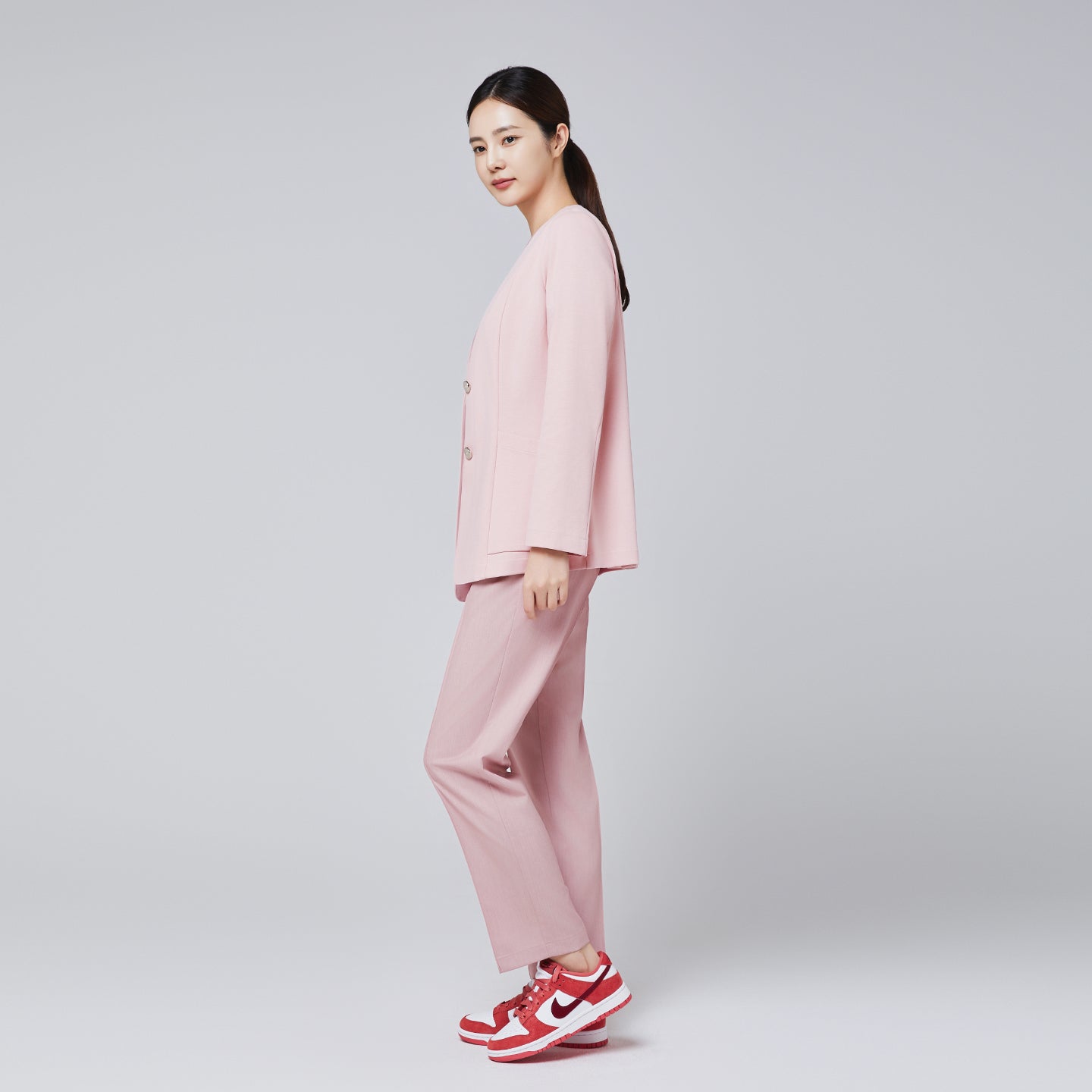 A woman dressed in a soft pink comfort cardigan and matching trousers, paired with red and white sneakers, posing sideways against a plain background,Soft Pink