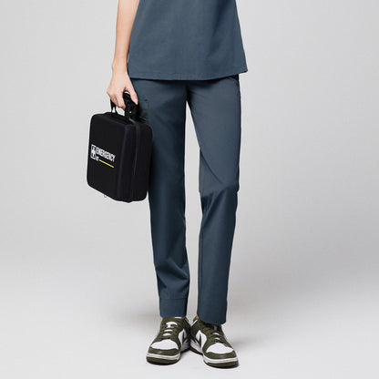 Smoky blue scrub pants with split hem and side pocket, holding a black emergency kit, paired with green and white sneakers,Smoky Blue