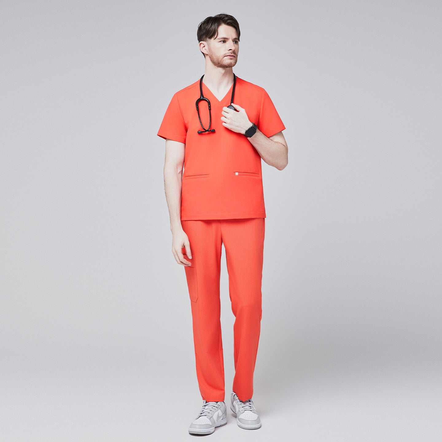 Man wearing tiger orange scrubs with a V-neck and double pockets, holding a black stethoscope, paired with white sneakers,Tiger Orange