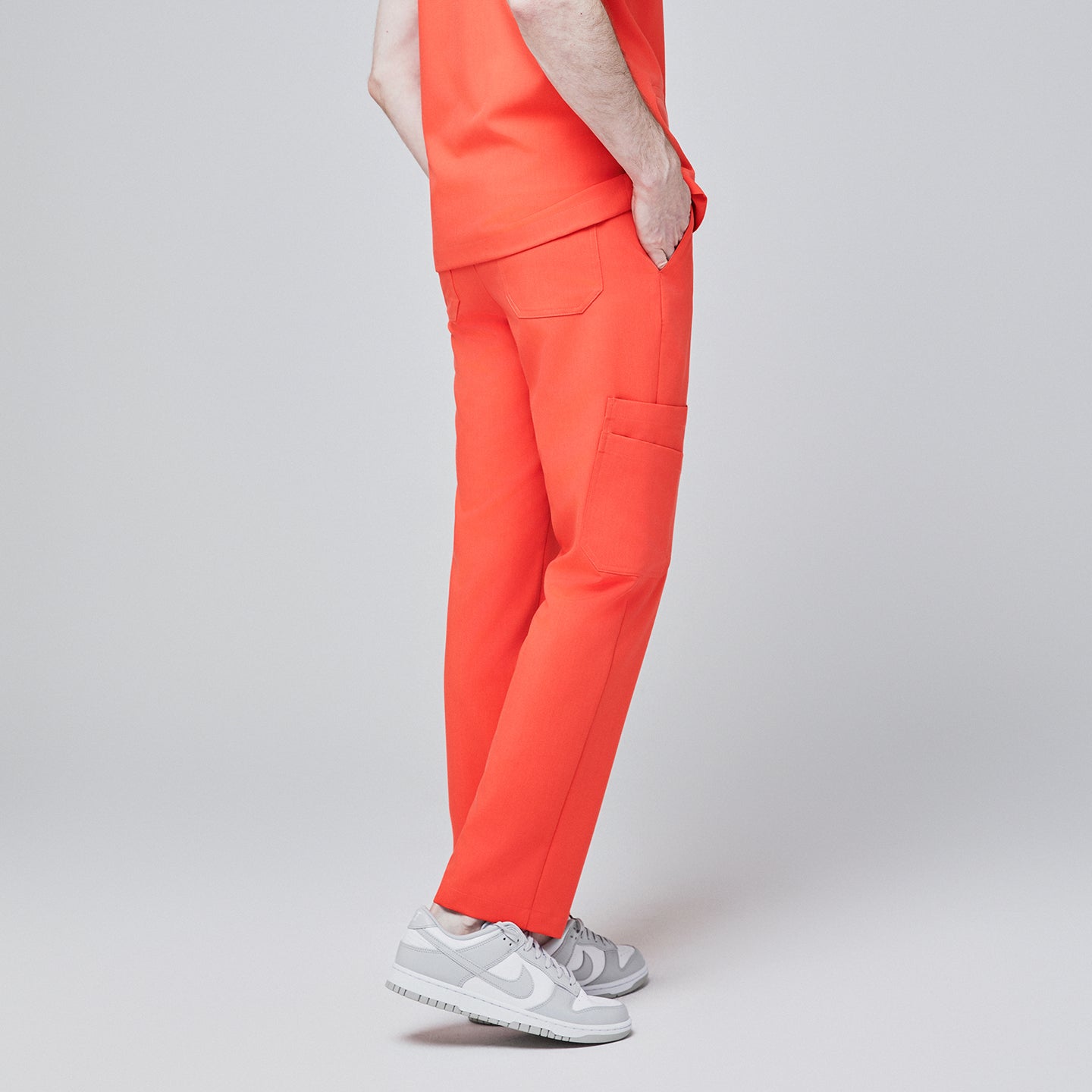 Side view of model wearing tiger orange scrub pants with a single side pocket and back flap pockets, paired with white sneakers, set against a light gray background,Tiger Orange