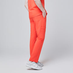 Image of Side view of model wearing tiger orange scrub pants with a single side pocket and back flap pockets, paired with white sneakers, set against a light gray background,Tiger Orange