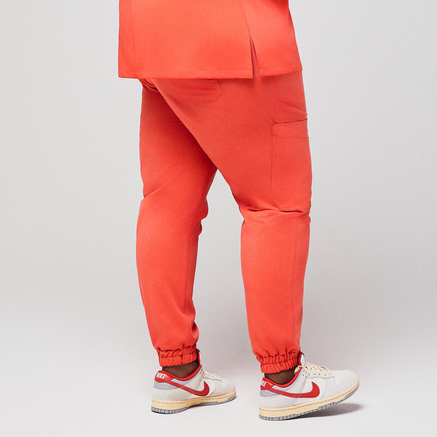 Back view of bright orange jogger scrub pants with elastic cuffs and side pockets, worn with white and red Nike sneakers,Tiger Orange