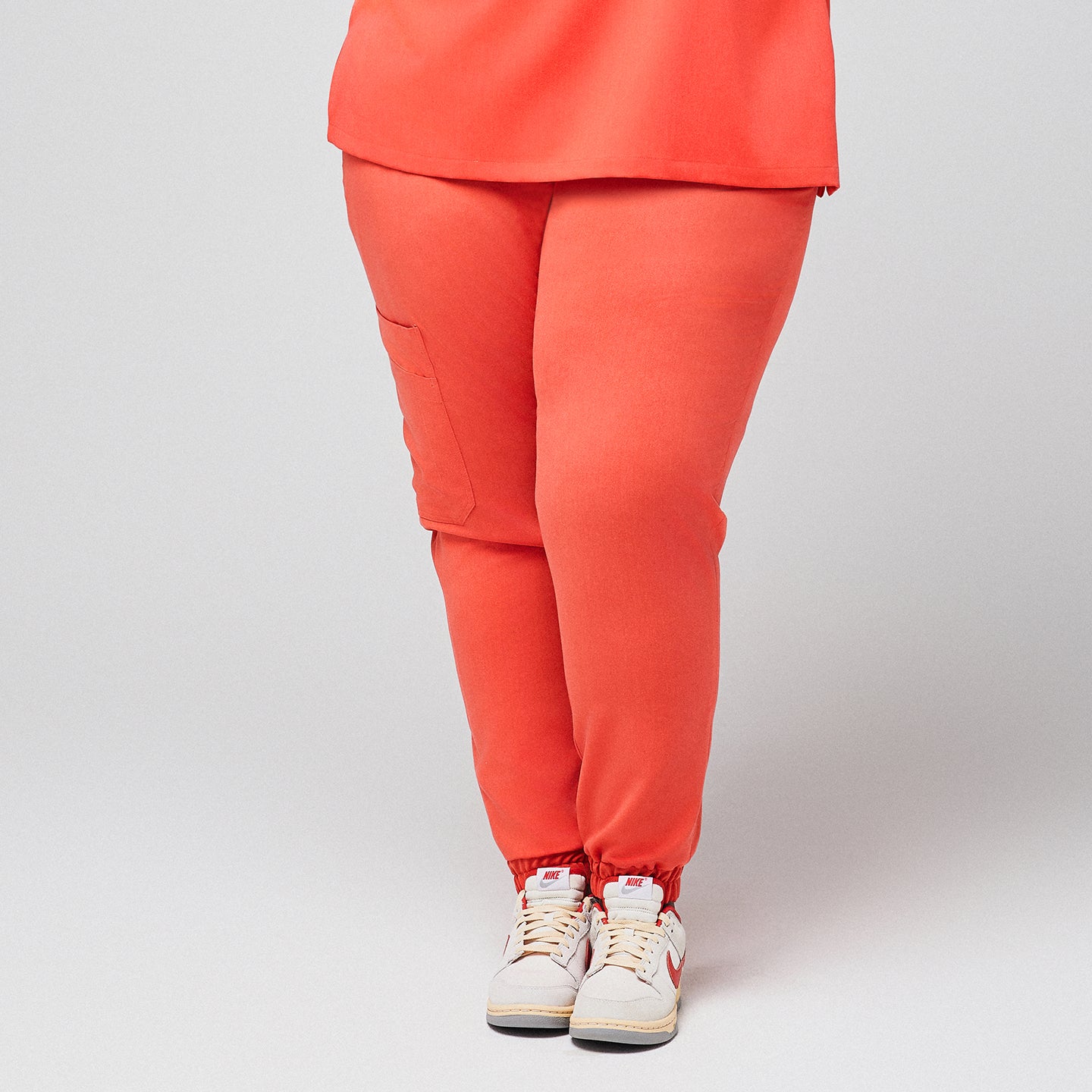 Close-up of bright orange jogger scrub pants with side pockets, paired with white and red Nike sneakers,Tiger Orange