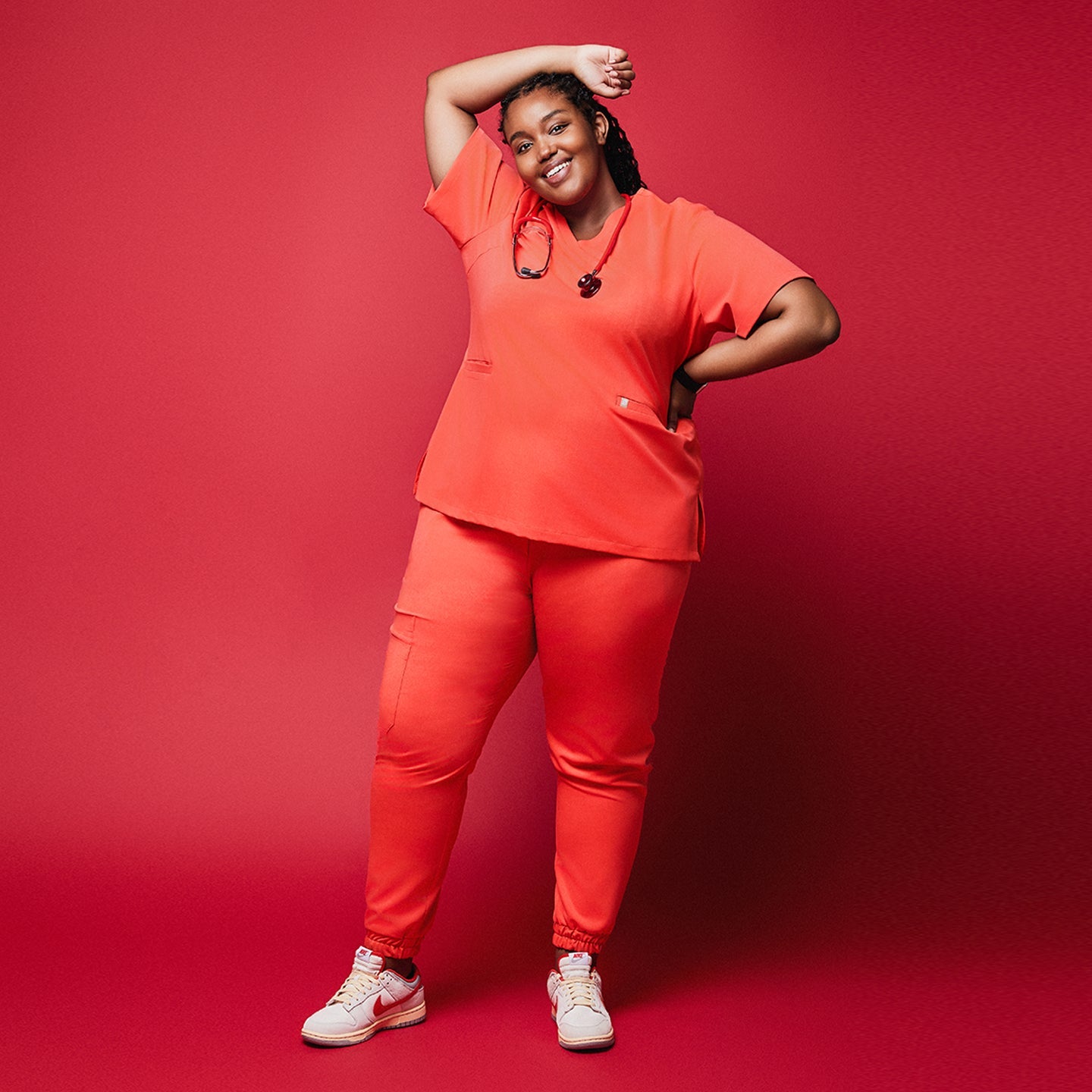 A woman posing in a Tiger Orange Double Pocket Scrub Top and Tiger Orange Straight Split Hem Scrub Pants, smiling with one arm raised,Tiger Orange