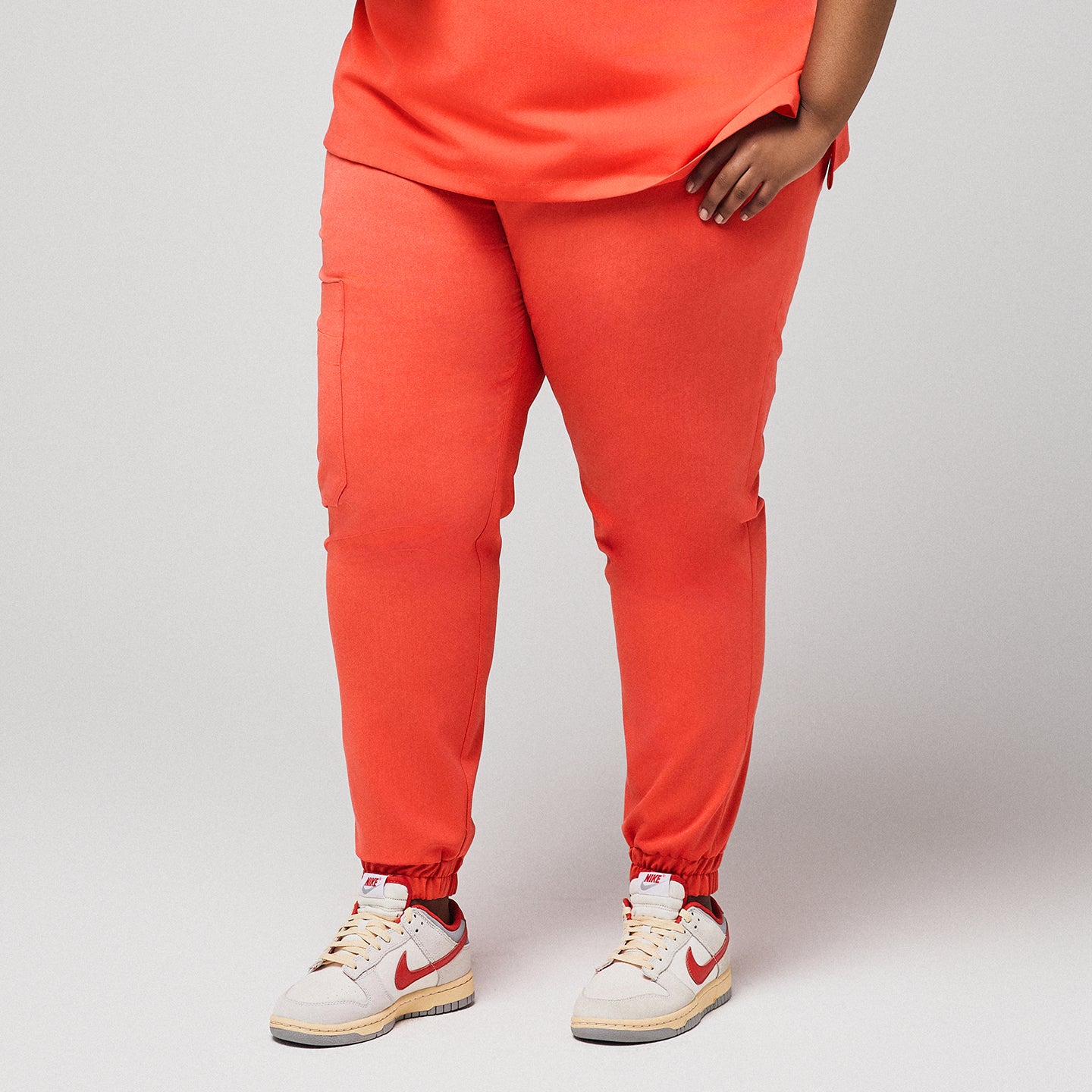 Front view of bright orange jogger scrub pants with side pockets, worn with white and red Nike sneakers,Tiger Orange