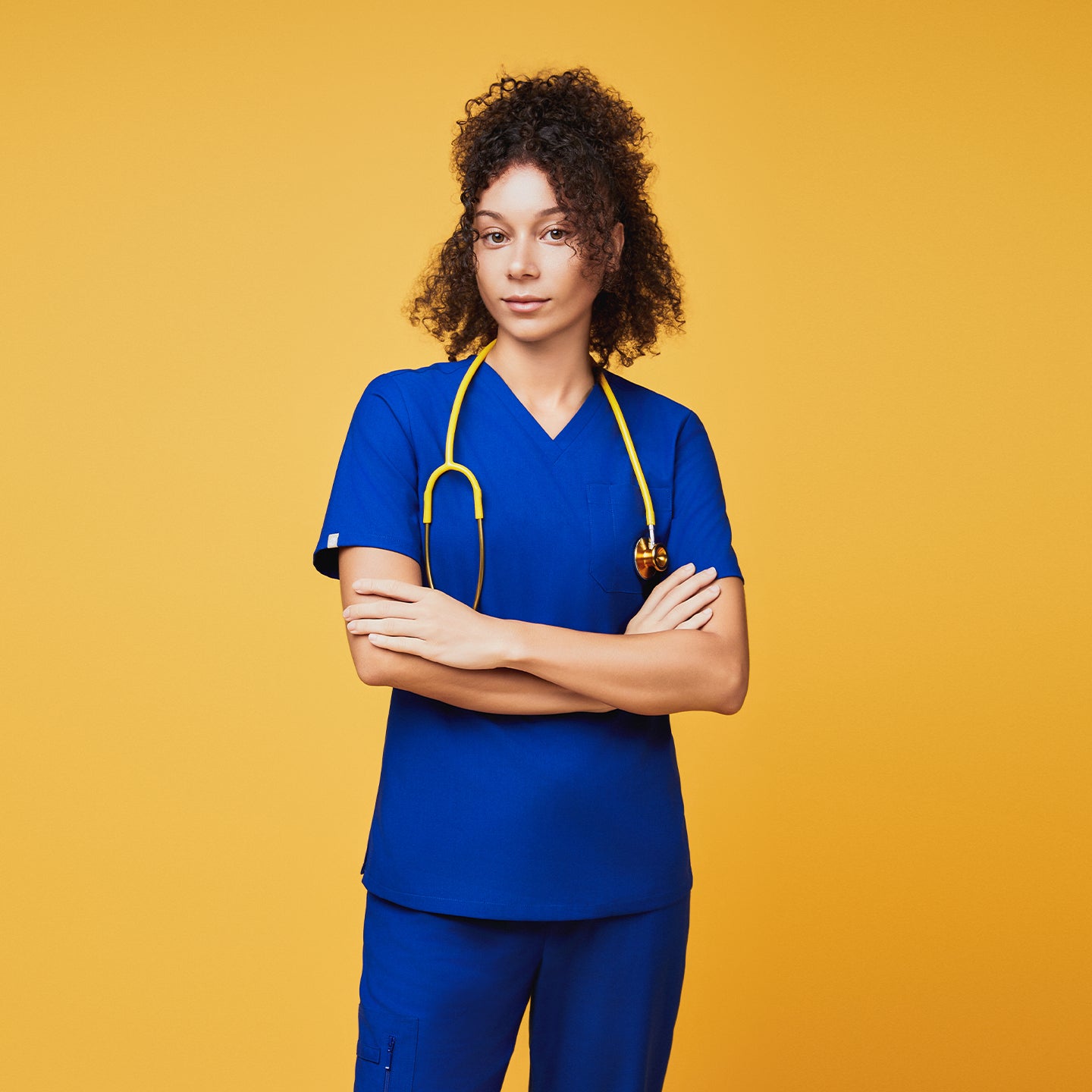 Model wearing Zenir royal blue 3-pocket scrub top with a yellow stethoscope against a yellow background,Royal Blue