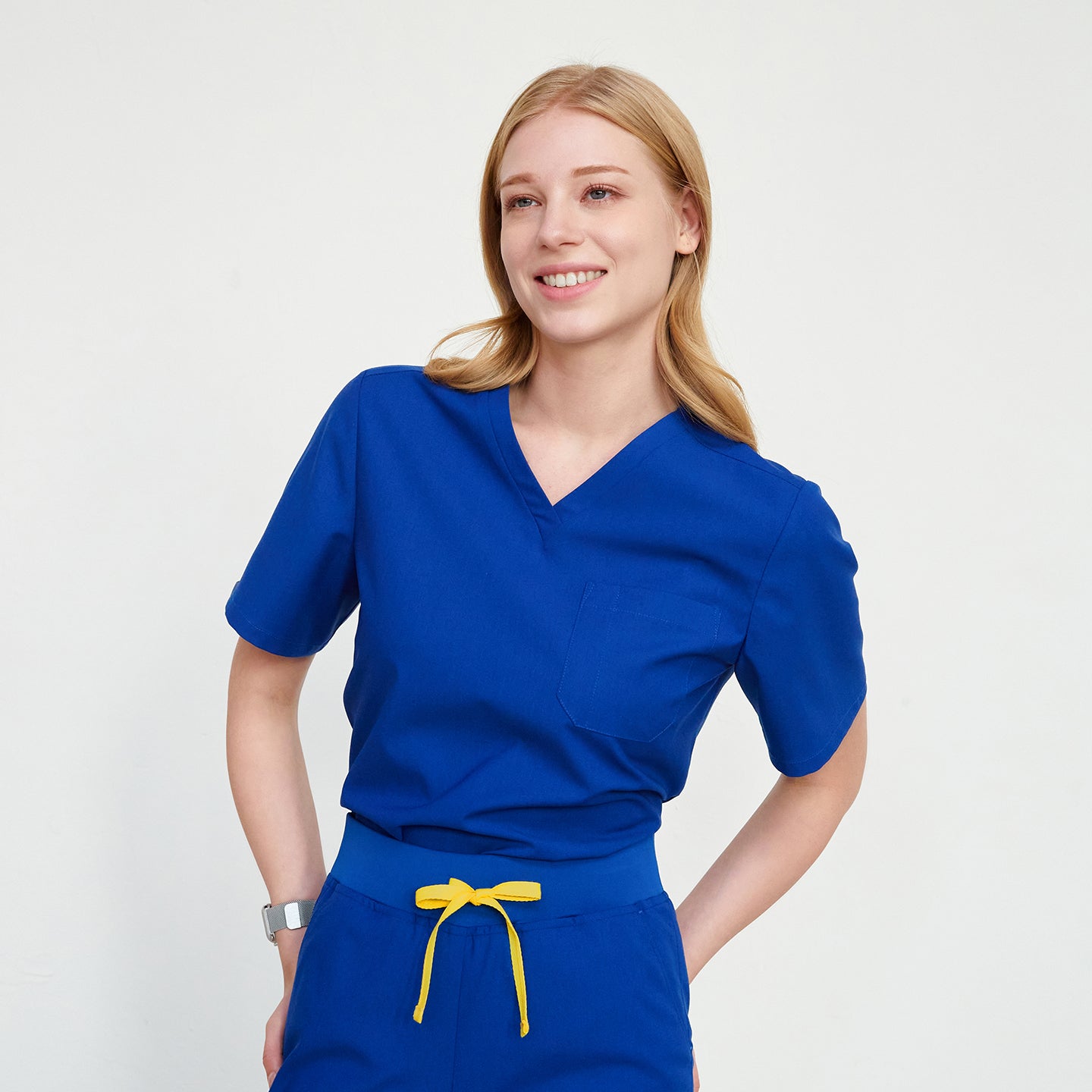 Blonde woman smiling, wearing a V-neck scrub top with a chest pocket, and matching pants with a yellow drawstring,Royal Blue