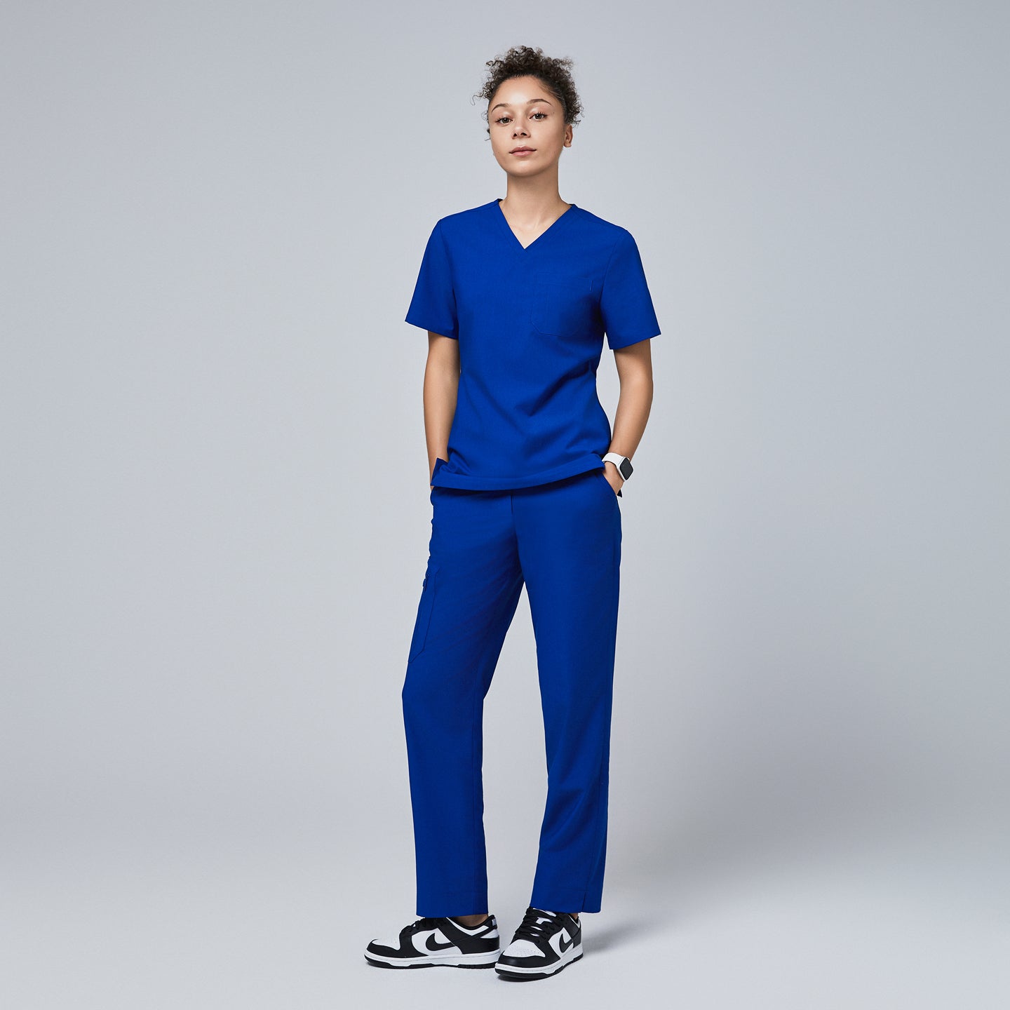 Model wearing Zenir royal blue 3-pocket scrub top and straight-leg scrub pants paired with black and white sneakers,Royal Blue