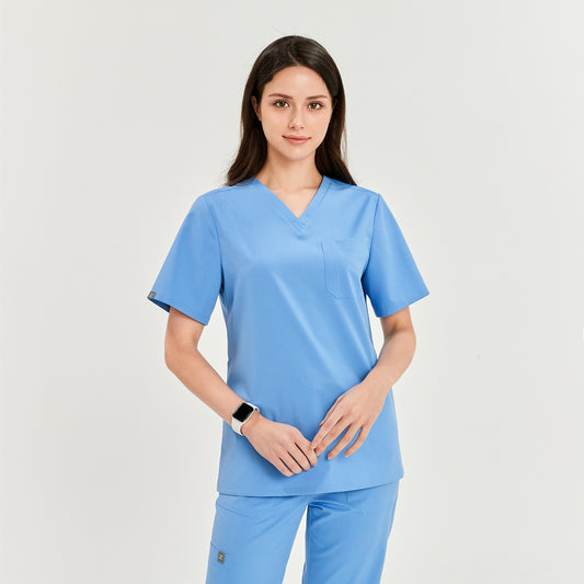 Woman wearing a V-neck scrub top and matching pants, hands together, looking directly at the camera, Ceil Blue