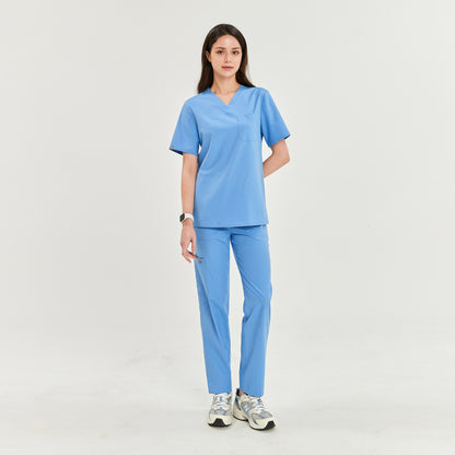 Woman standing in a V-neck scrub top and matching pants, hands at her sides, and looking straight ahead, Ceil Blue