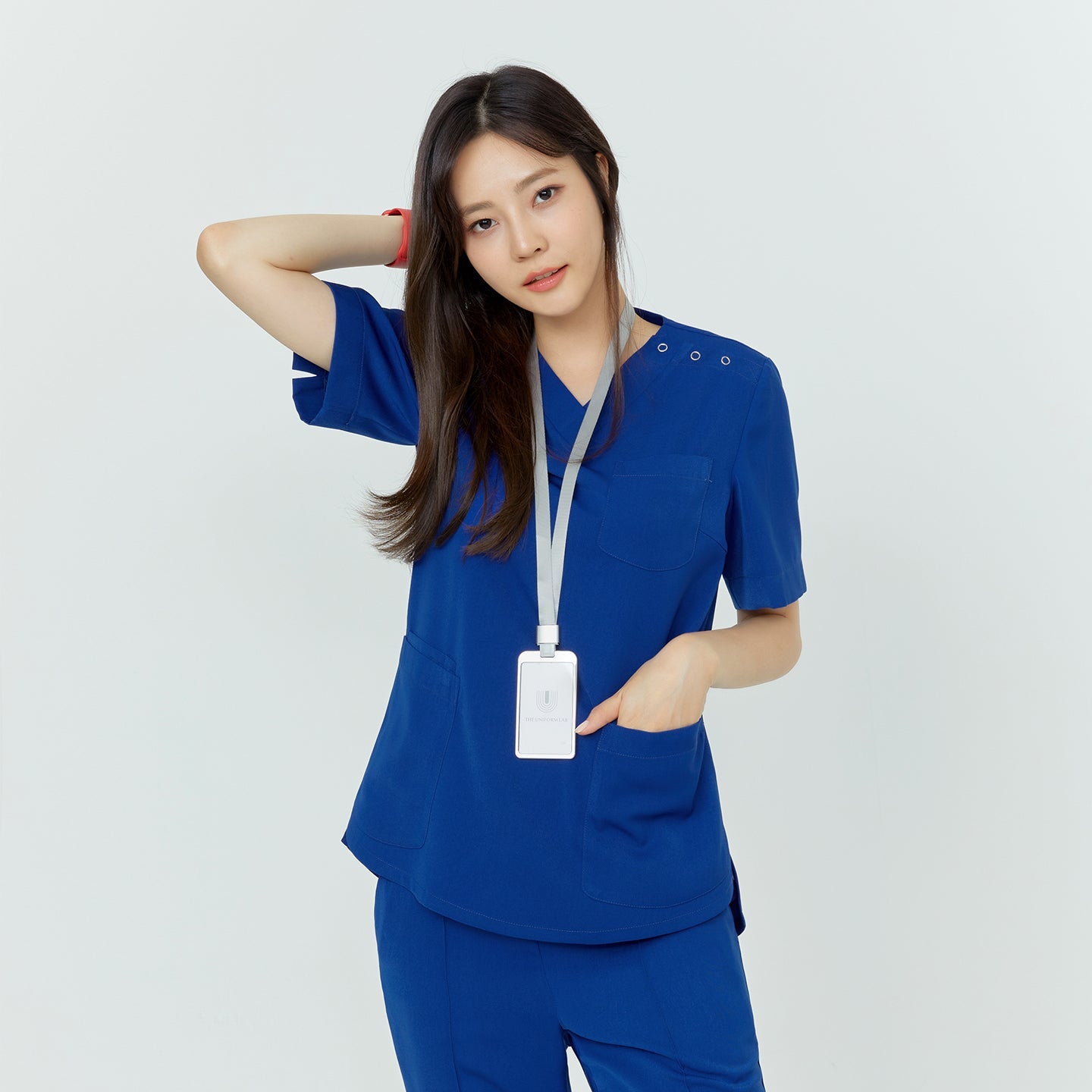 Woman in medical scrubs, standing with one hand in her pocket and the other behind her head,Royal Blue