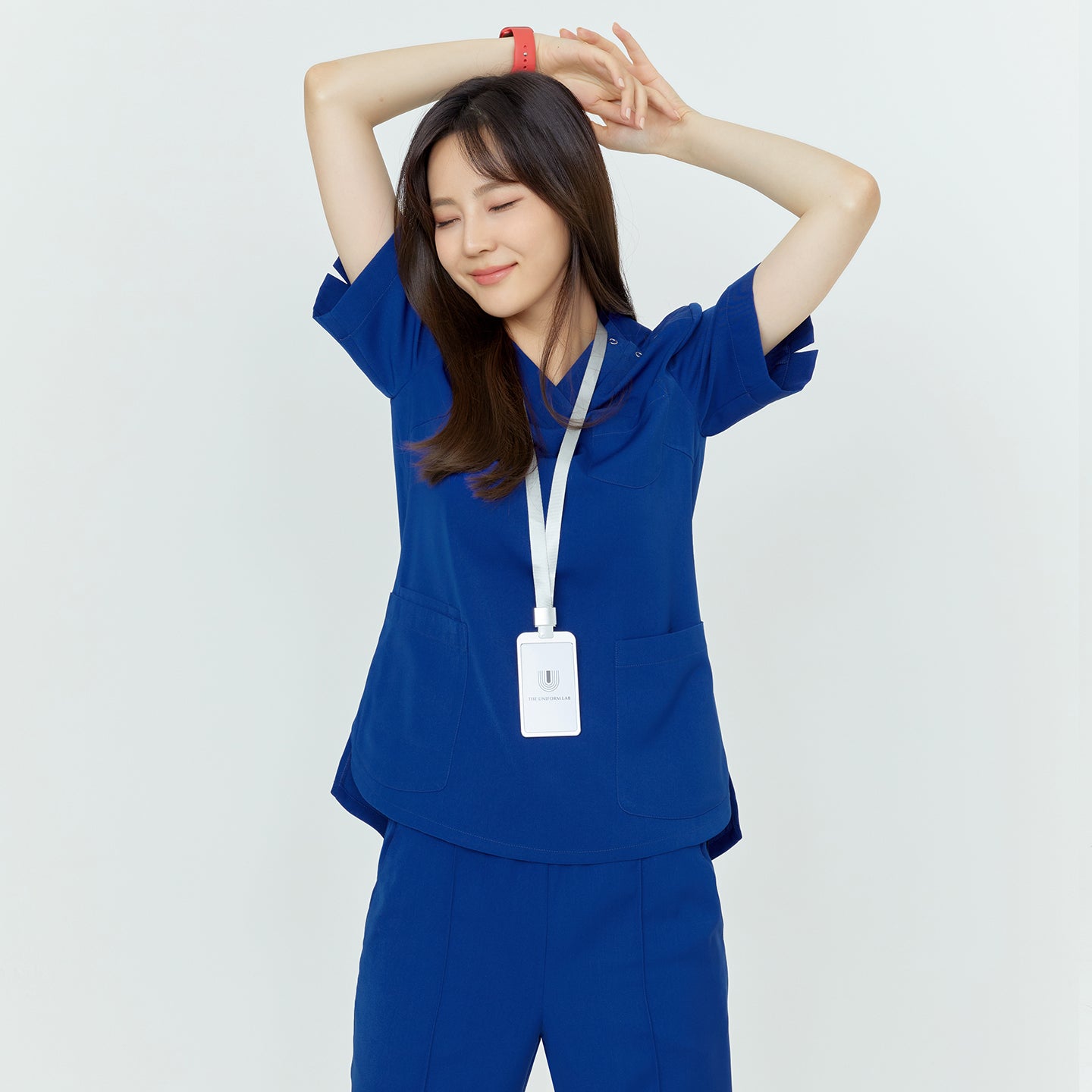Woman in medical scrubs, stretching with arms above her head, smiling with eyes closed,Royal Blue