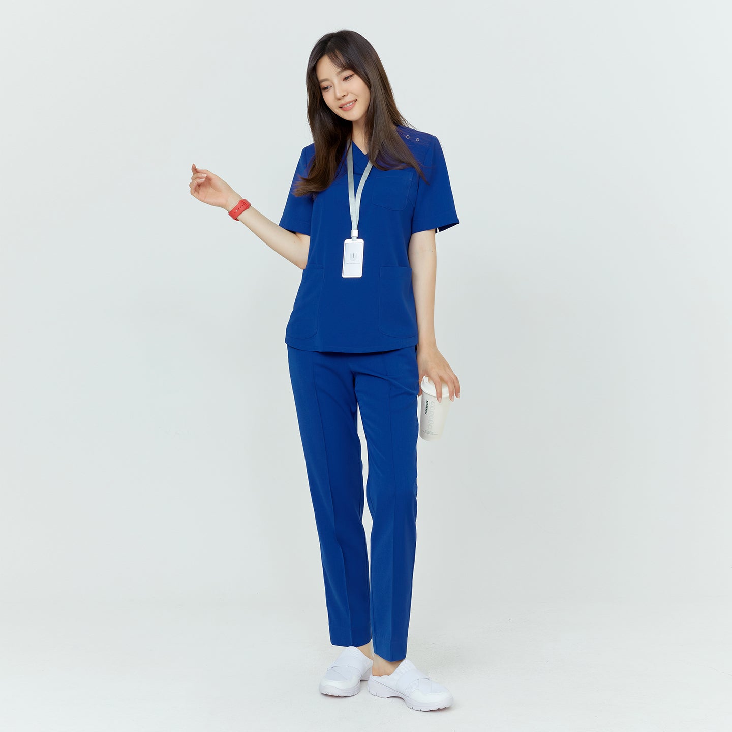 Woman in medical scrubs with a lanyard, standing and holding a drink, smiling with her eyes closed,Royal Blue