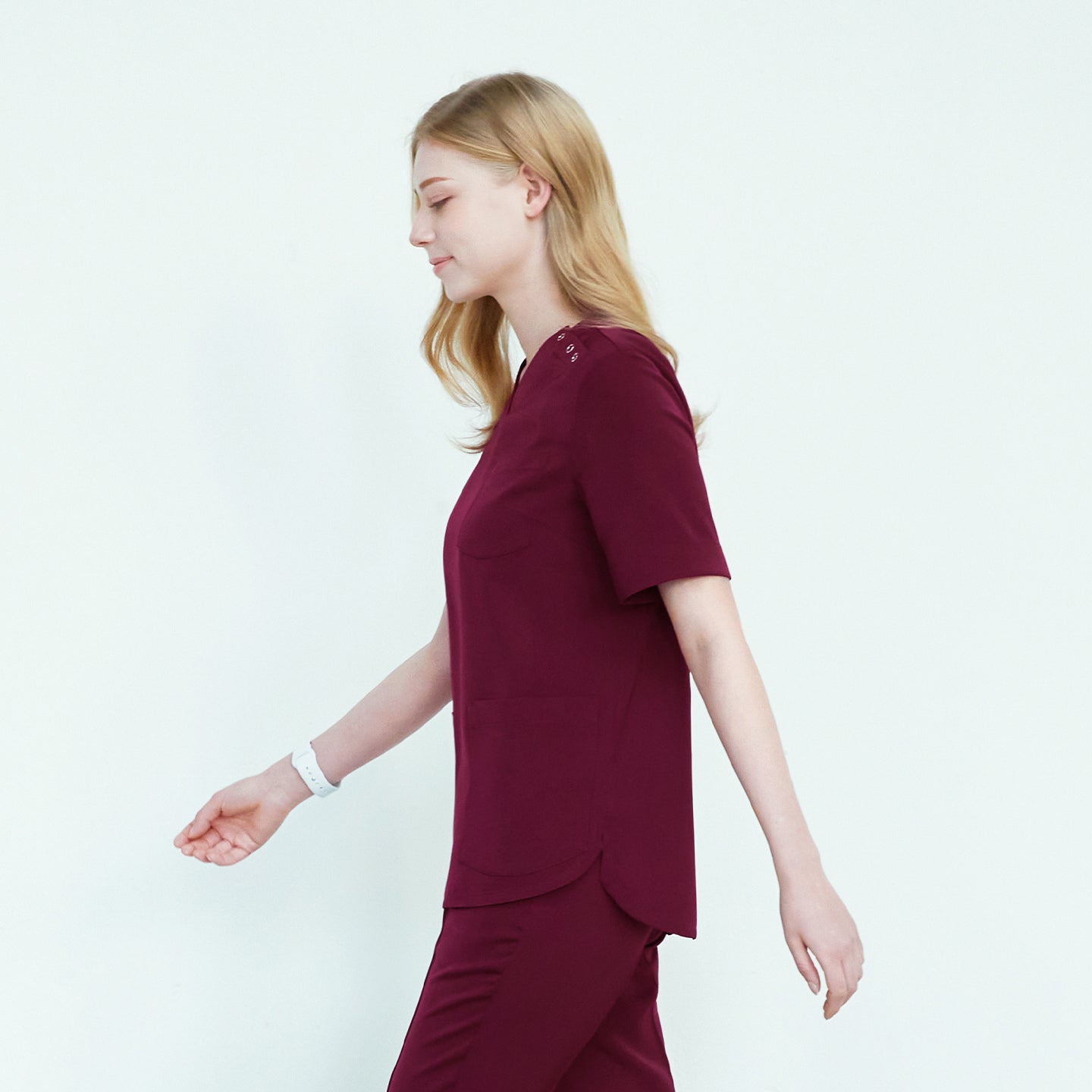 Woman walking sideways in 3-button scrub top with two front pockets and matching pants,Burgundy