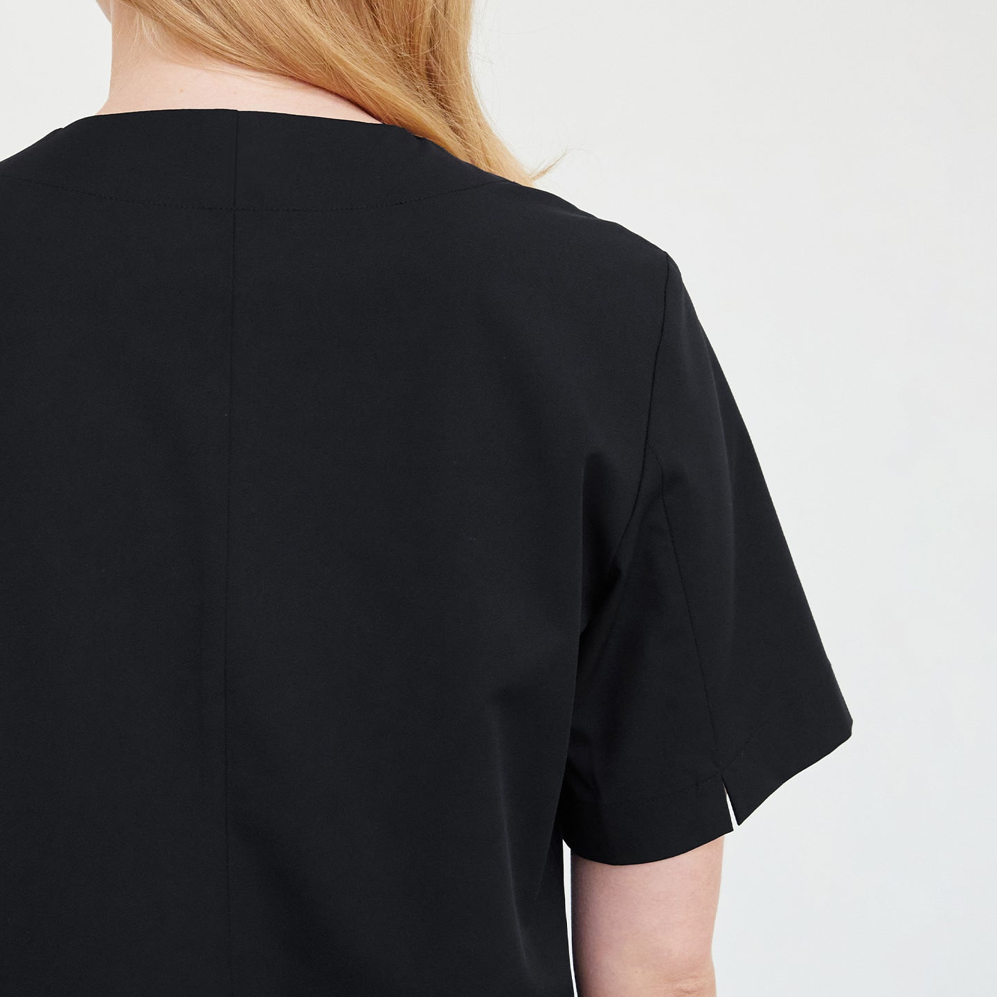 Back detail of a woman wearing a black scrub top, showing the stitching and fabric texture,Black