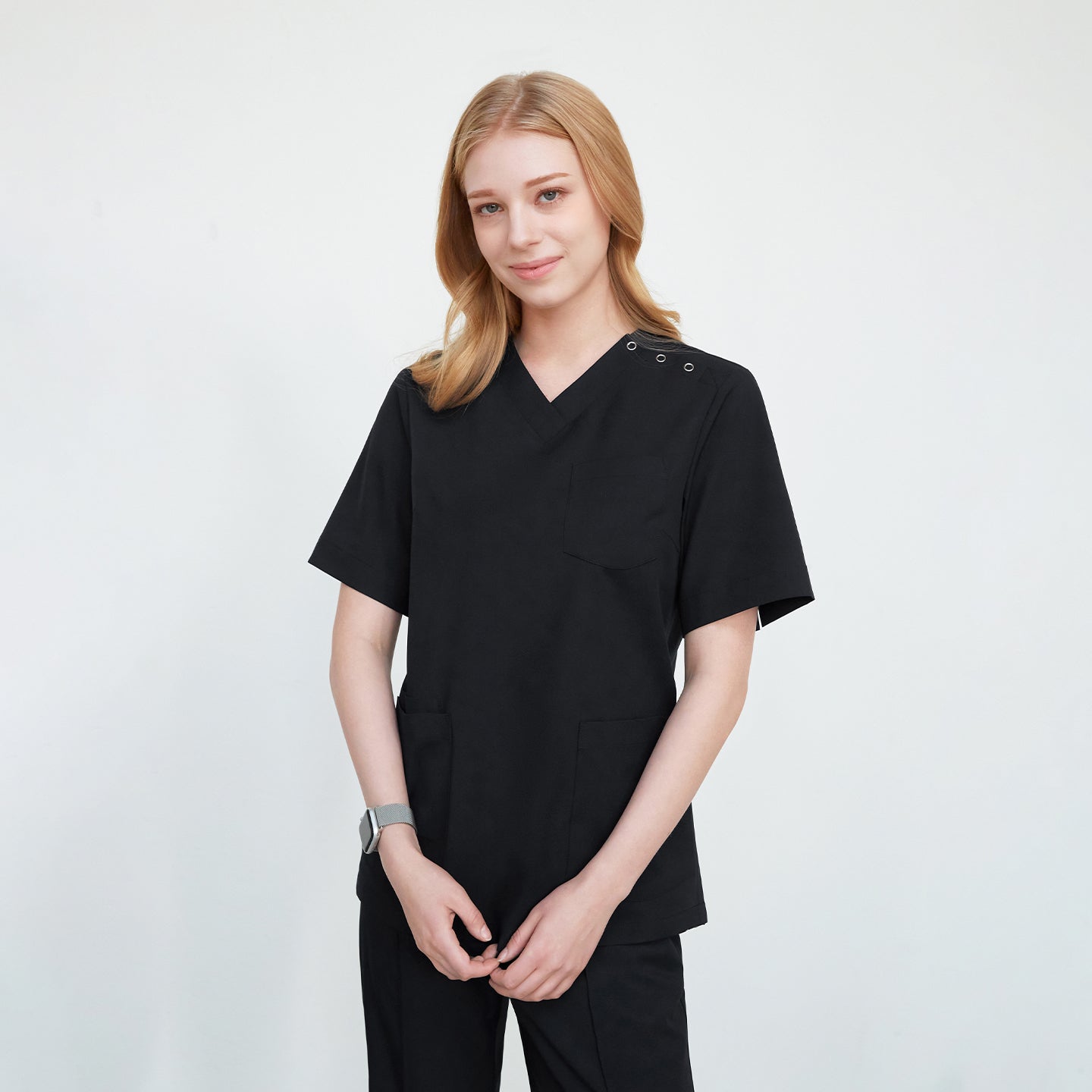 A woman wearing a black scrub top with buttons on the shoulder, standing against a plain background,Black