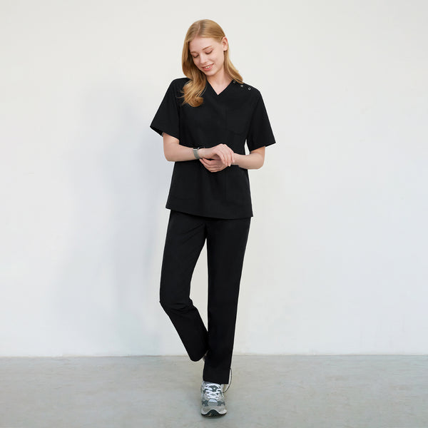 Woman in black Zenir scrub top with three shoulder buttons and matching pants, smiling, full-body view,Black