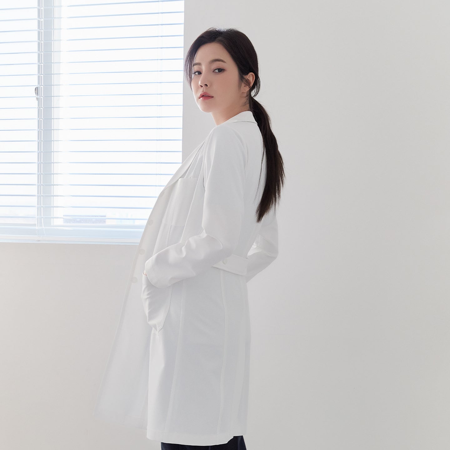 Woman in Zenir White Long Lab Coat LCW-04, side view with hands in pockets, belted back detail,White