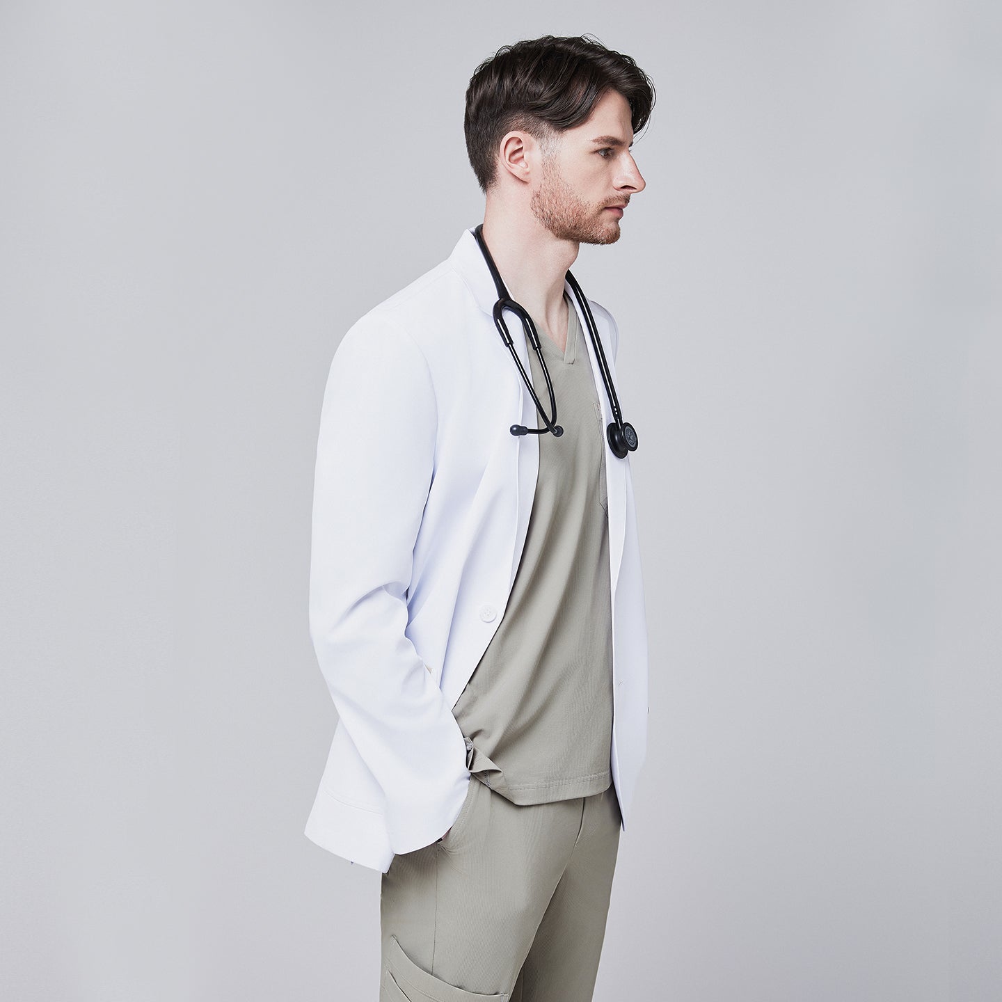 Side view of a male model wearing a white short lab coat over olive green scrub pants, showcasing clean and tailored design,White