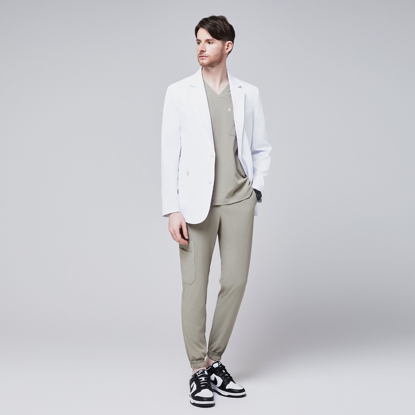 Male model wearing a white short lab coat over an olive green scrub set, styled with black and white sneakers,White