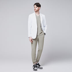 Image of Male model wearing a white short lab coat over an olive green scrub set, styled with black and white sneakers,White