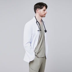 Image of Male model in a white short lab coat over an olive green scrub set, posing in a profile view with hands in pockets,White