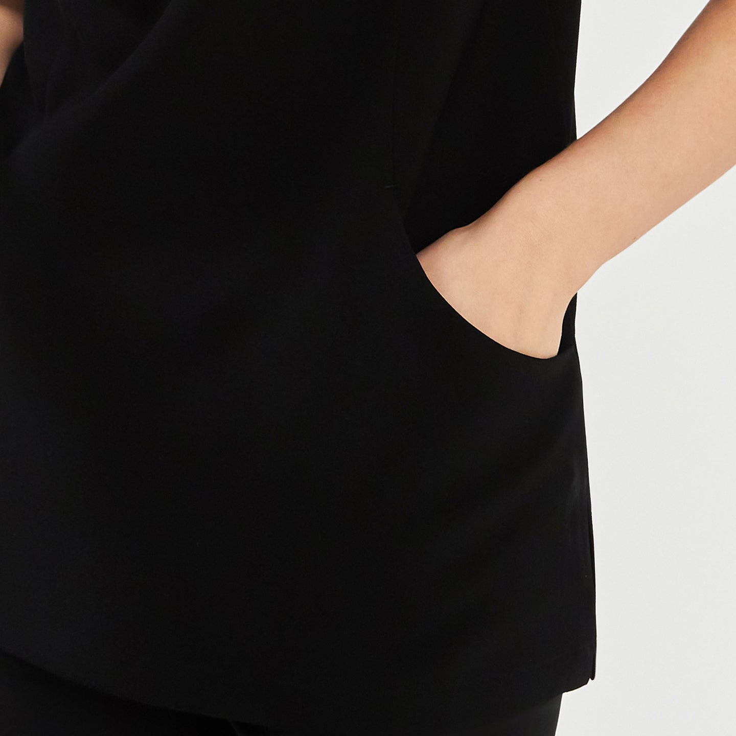 Close-up of a woman wearing a black soft stretch scrub top, showing her hand in the side pocket detail,Black