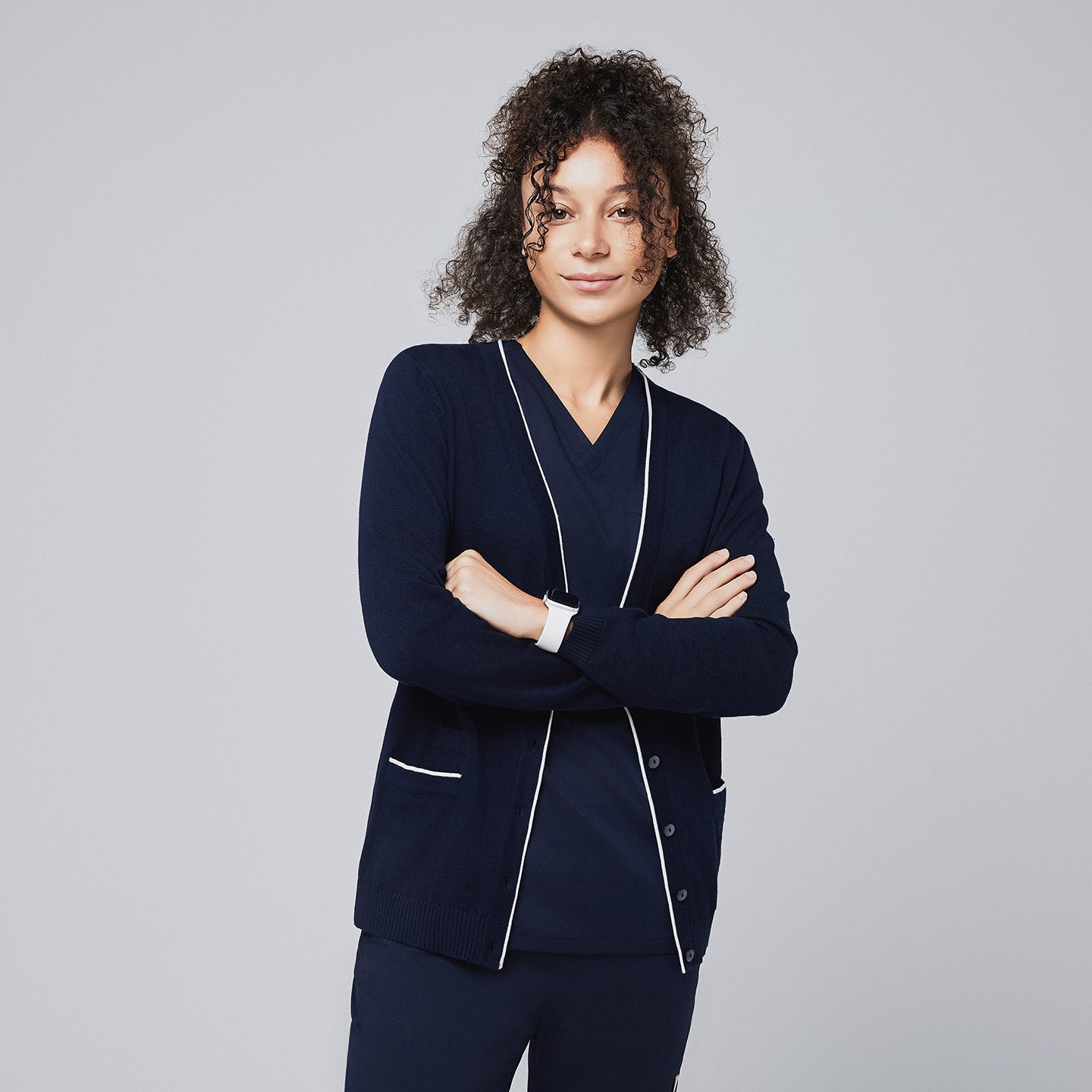 Confident woman wearing a navy scrub set paired with a navy cardigan featuring white trim, standing with arms crossed,Navy