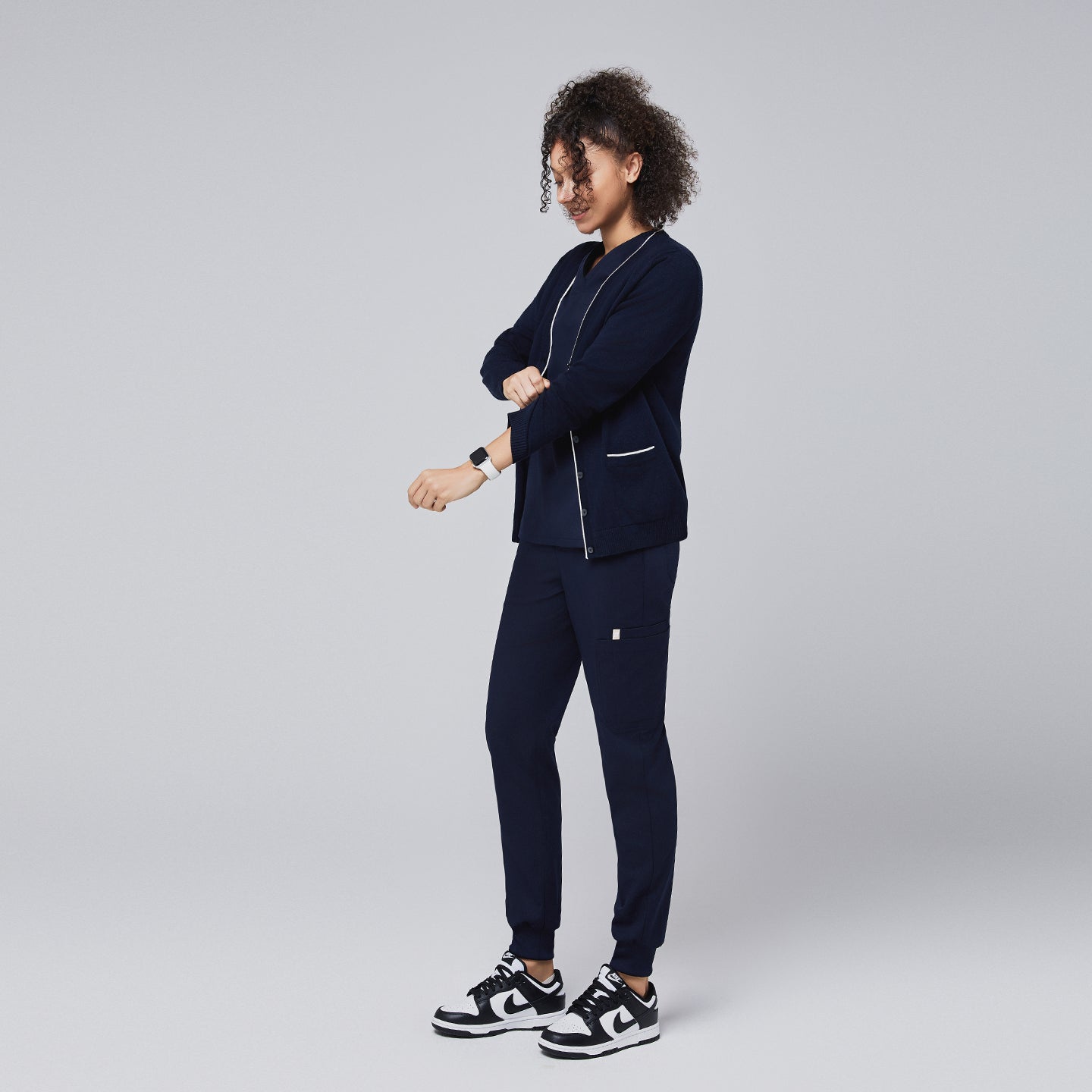 Woman in a navy scrub set and navy cardigan with white trim adjusting her sleeve, showcasing a professional yet relaxed look,Navy