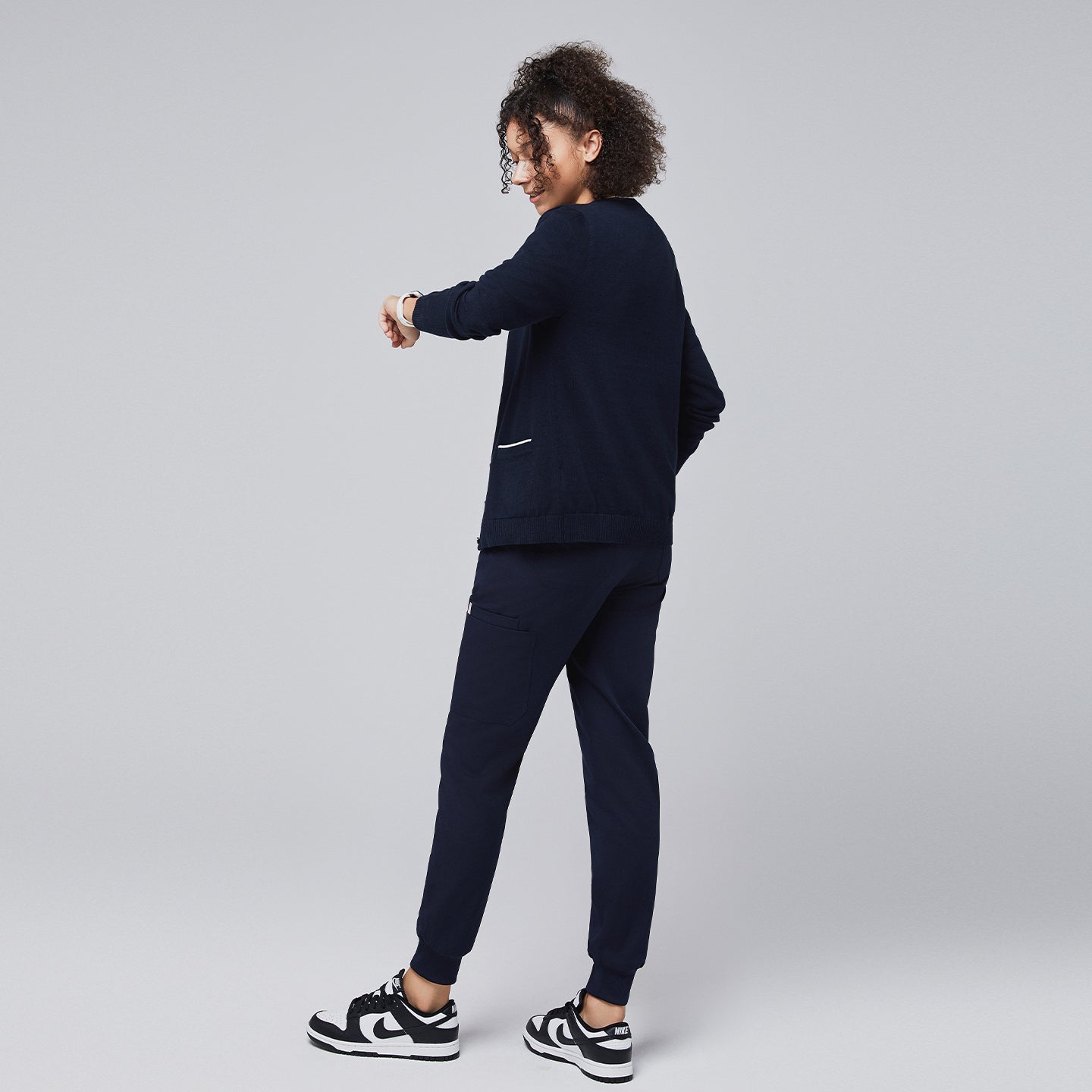 Woman in a navy scrub set and navy cardigan with white trim adjusting her sleeve, showcasing a professional yet relaxed look,Navy