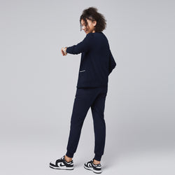 Image of Woman in a navy scrub set and navy cardigan with white trim adjusting her sleeve, showcasing a professional yet relaxed look,Navy