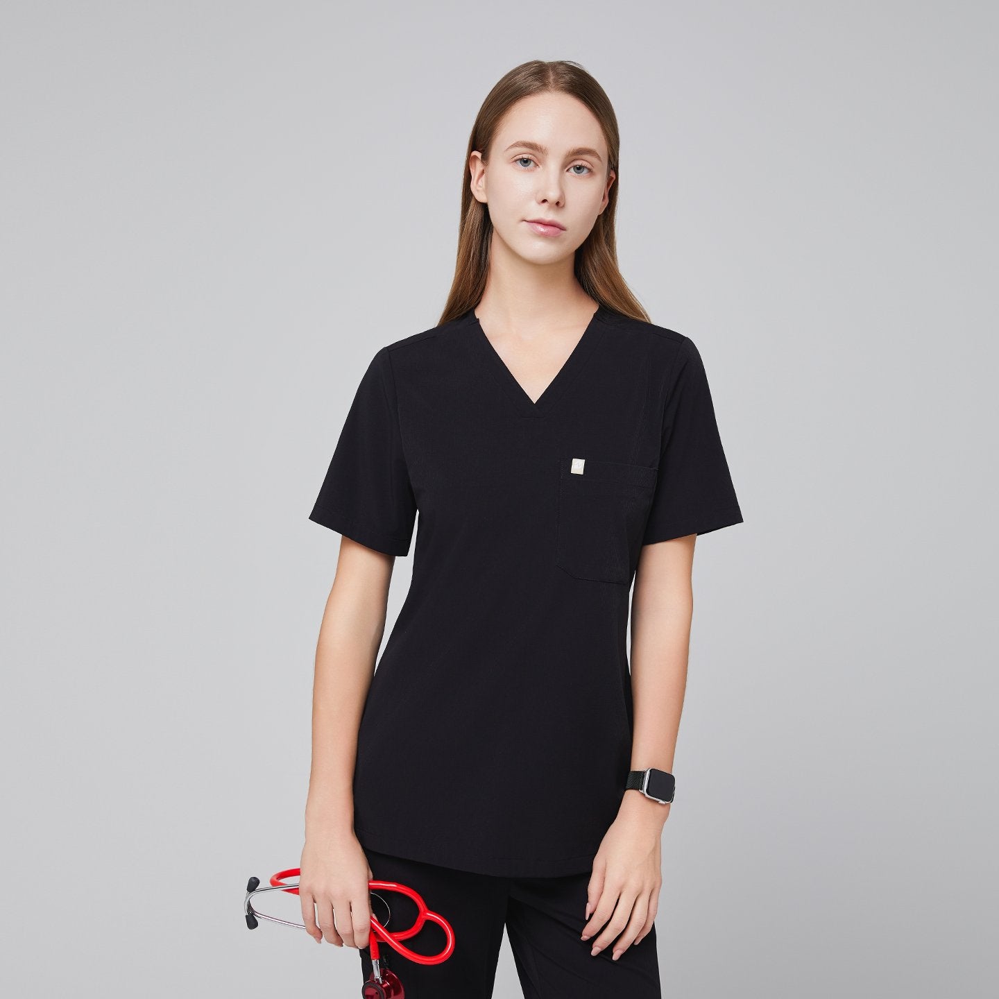 A woman wearing a Midnight Black Single Pocket Scrub Top with short sleeves, holding a red stethoscope,Midnight Black